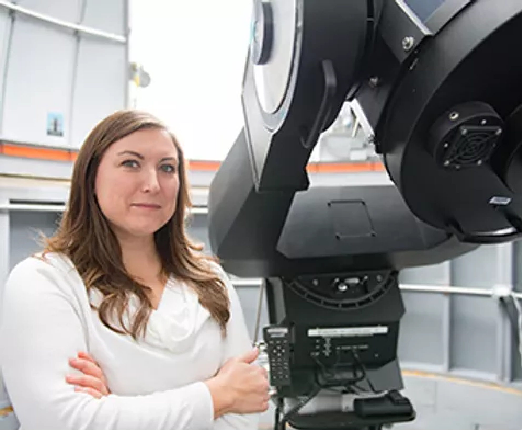 Bio headshot of Lindsay Fuller. Her arms are crossed and she stands in front of a large telescope.